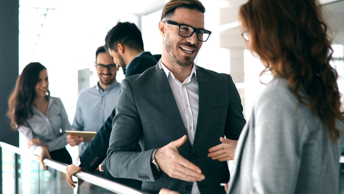 Business professionals shaking hands and smiling in a modern office setting, symbolizing positive collaboration.