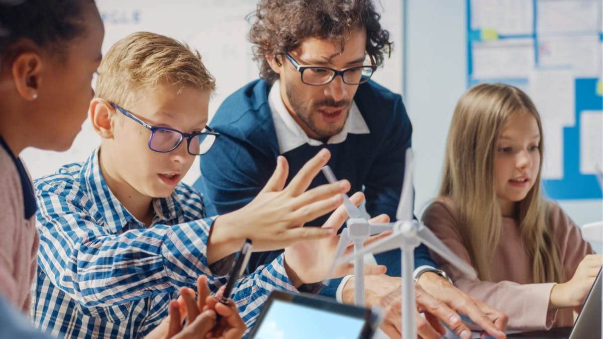 Group of students working on a wind turbine project, assisted by their teacher in a classroom setting.